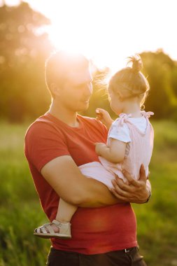 Mutlu baba ve küçük kız gün batımında yaz parkında eğleniyorlar. Babam güneşli arazide küçük bir çocukla oynuyor. Baba ve kızının öpücükleri ve kucaklamaları. Aile ve babalık kavramı.