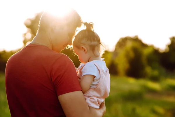 Happy dad and little baby girl  having fun in summer park at sunset. Dad plays with small child on sunny field. Kisses and hugs of father and daughter. Family  and fatherhood concept.