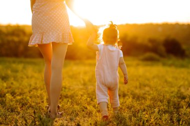 Anne ve küçük kızı gün batımında bir yaz parkında birlikte oynuyorlar. Küçük çocuklu mutlu bir anne güneşli bir alanda eğleniyor. Öpücükler ve sarılmalar. Mutlu aile kavramı.. 