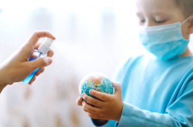 Gezegen sterilizasyonu. Dünya küresi tutan steril tıbbi maskeli bir çocuk. Gezegeni kurtar. Salgın koronavirüsün yayılmasını önleme konsepti.