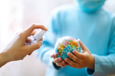 Gezegen sterilizasyonu. Dünya küresi tutan steril tıbbi maskeli bir çocuk. Gezegeni kurtar. Salgın koronavirüsün yayılmasını önleme konsepti.