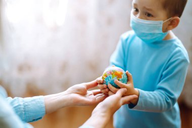 Koruyucu steril tıbbi maskeli bir çocuk ve elinde dünya küresi olan bir anne. Gezegeni kurtar. Salgın koronavirüsün yayılmasını önleme konsepti.