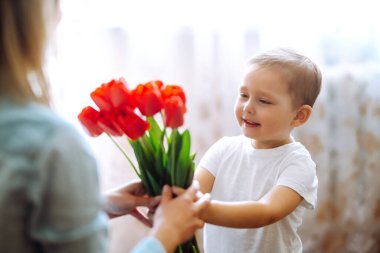 Küçük oğlu annesini tebrik ediyor ve bir buket çiçek lalesi veriyor. Anneler Günün kutlu olsun. Aile tatili ve birliktelik.