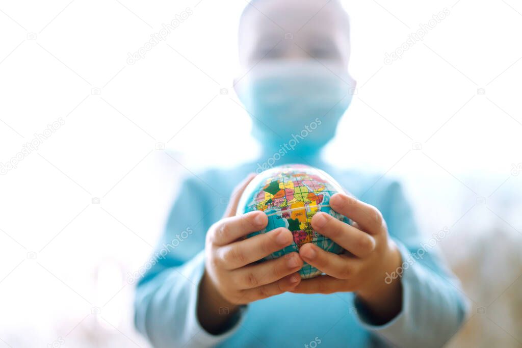 Child in protective sterile medical mask holding a world globe. Save planet. The concept of preventing the spread of the epidemic coronavirus.