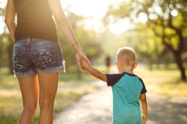 Gün batımında anne ve çocuğun ellerine yakın çekim yap. Anne ve oğlu parkta yürüyor. Aile tatili ve birliktelik. Yaz konsepti.