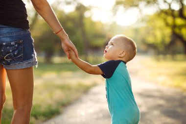 Gün batımında anne ve çocuğun ellerine yakın çekim yap. Anne ve oğlu parkta yürüyor. Aile tatili ve birliktelik. Yaz konsepti.