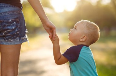 Gün batımında anne ve çocuğun ellerine yakın çekim yap. Anne ve oğlu parkta yürüyor. Aile tatili ve birliktelik. Yaz konsepti.