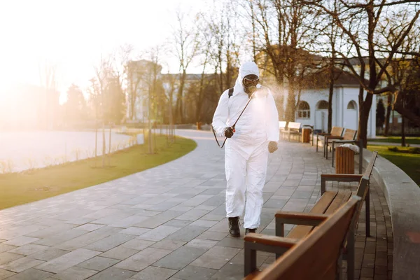 Man wearing protective suit disinfecting public places in the sun with spray chemicals to preventing the spread of coronavirus, pandemic in quarantine city. Covid -19. Cleaning concept.