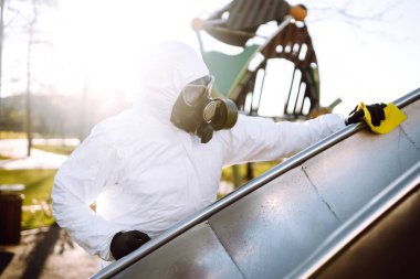 Koruyucu kıyafet giyen adam karantina şehrinde salgın olan koronavirüsün yayılmasını önlemek için oyun alanını temizliyor ve dezenfekte ediyor. Covid -19. Temizlik ve Dezenfeksiyon.