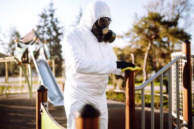 Koruyucu kıyafet giyen adam karantina şehrinde salgın olan koronavirüsün yayılmasını önlemek için oyun alanını temizliyor ve dezenfekte ediyor. Covid -19. Temizlik ve Dezenfeksiyon.