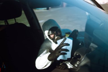 Koruyucu giysili Adam 'ın eli arabadaki direksiyon simidini yıkıyor ve dezenfekte ediyor, Covid-19 virüsü enfeksiyonunu önlüyor, mikrop veya bakteri bulaşmasını önlüyor.