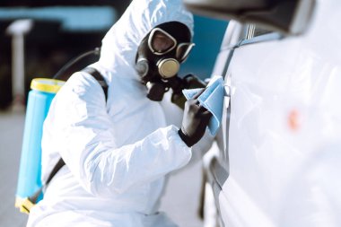 Korunaklı giysiler içindeki bir adamın eli araba yıkama ve dezenfeksiyon tutacağı, Coronavirüs salgınının yayılmasını önlemek için, karantina şehrinde salgın.. 