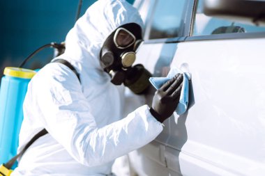 Korunaklı giysiler içindeki bir adamın eli araba yıkama ve dezenfeksiyon tutacağı, Coronavirüs salgınının yayılmasını önlemek için, karantina şehrinde salgın.. 