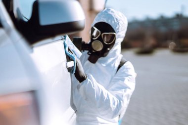 Korunaklı giysiler içindeki bir adamın eli araba yıkama ve dezenfeksiyon tutacağı, Coronavirüs salgınının yayılmasını önlemek için, karantina şehrinde salgın.. 