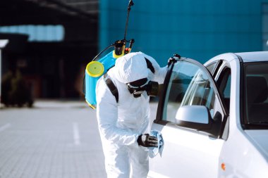 Korunaklı kıyafet yıkayan ve araba dezenfekte eden bir adam, koronavirüs salgınının yayılmasını önlemek için, karantina şehrinde salgın. Covid 19.