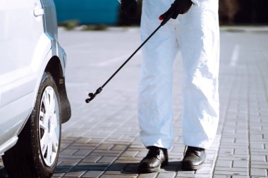 Korunaklı kıyafet yıkayan ve araba tekerleklerini dezenfekte eden adam Coronavirus salgınının yayılmasını önlemek için, karantina şehrinde salgın. Covid 19.