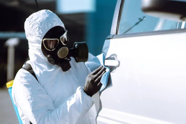 Hand of Man in protective suit washing and disinfection handles of a car, to preventing the spread of the epidemic of coronavirus, pandemic in quarantine city.