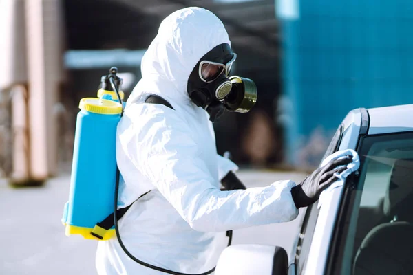 Man in protective suit washing and disinfection handles of a car, to preventing the spread of the epidemic of coronavirus, pandemic in quarantine city. Covid-19.