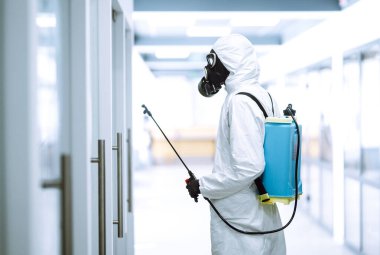 COVID-19 'u önlemek için ofisin dezenfekte edilmesi, karantina şehrinde pandemik olan koronavirüsün yayılmasını önlemek için koruyucu koruyucu kimyasal madde kullanan adam. Temizlik kavramı.