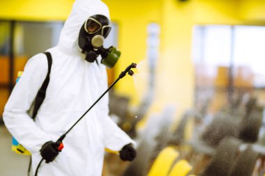 Korunaklı kıyafet giyen bir adam karantina şehrinde koronavirüsün yayılmasını önlemek için toplantı salonunu sprey kimyasallarla dezenfekte ediyor. Ofisin dezenfekte edilmesi. COVID-19.