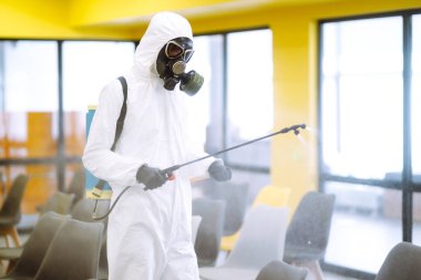 Korunaklı kıyafet giyen bir adam karantina şehrinde koronavirüsün yayılmasını önlemek için toplantı salonunu sprey kimyasallarla dezenfekte ediyor. Ofisin dezenfekte edilmesi. COVID-19.