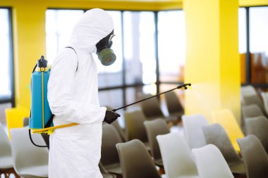 Korunaklı kıyafet giyen bir adam karantina şehrinde koronavirüsün yayılmasını önlemek için toplantı salonunu sprey kimyasallarla dezenfekte ediyor. Ofisin dezenfekte edilmesi. COVID-19.