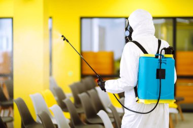 Korunaklı kıyafet giyen bir adam karantina şehrinde koronavirüsün yayılmasını önlemek için toplantı salonunu sprey kimyasallarla dezenfekte ediyor. Ofisin dezenfekte edilmesi. COVID-19.