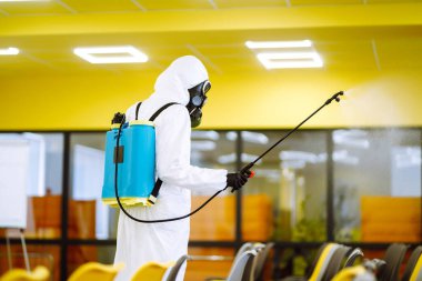 Korunaklı kıyafet giyen bir adam karantina şehrinde koronavirüsün yayılmasını önlemek için toplantı salonunu sprey kimyasallarla dezenfekte ediyor. Ofisin dezenfekte edilmesi. COVID-19.