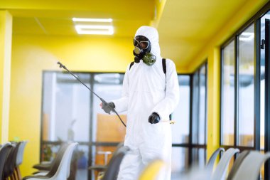 Korunaklı kıyafet giyen bir adam karantina şehrinde koronavirüsün yayılmasını önlemek için toplantı salonunu sprey kimyasallarla dezenfekte ediyor. Ofisin dezenfekte edilmesi. COVID-19.