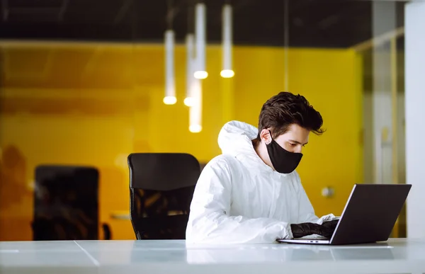 防護服の男とマスクは 空のオフィスでコンピュータ上で動作します コロナウイルスの拡散を防ぐための概念 隔離都市でのパンデミック Covid — ストック写真