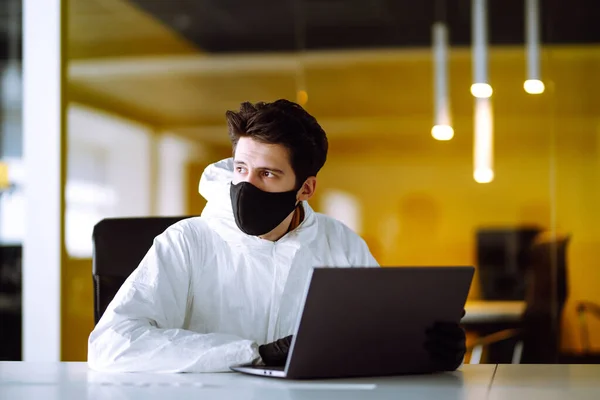 防護服の男とマスクは 空のオフィスでコンピュータ上で動作します コロナウイルスの拡散を防ぐための概念 隔離都市でのパンデミック Covid — ストック写真
