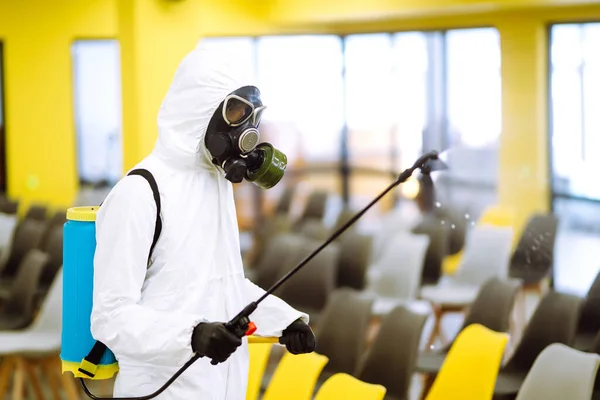 コロナウイルスの拡散を防ぐためにスプレー化学薬品で組立ホールを消毒保護スーツを身に着けている男 検疫都市のパンデミック オフィスの消毒 Covid — ストック写真