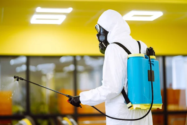 コロナウイルスの拡散を防ぐためにスプレー化学薬品で組立ホールを消毒保護スーツを身に着けている男 検疫都市のパンデミック オフィスの消毒 Covid — ストック写真