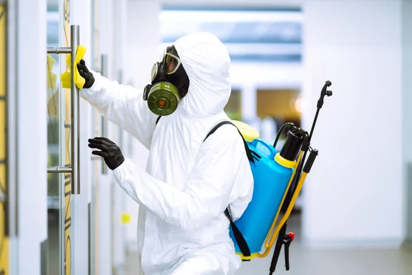 Man in protective hazmat suit washes door handles in office to preventing the spread of coronavirus, pandemic in quarantine city. Cleaning and disinfection of office. Covid-19.