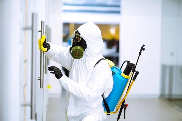 Man in protective hazmat suit washes door handles in office to preventing the spread of coronavirus, pandemic in quarantine city. Cleaning and disinfection of office. Covid-19.