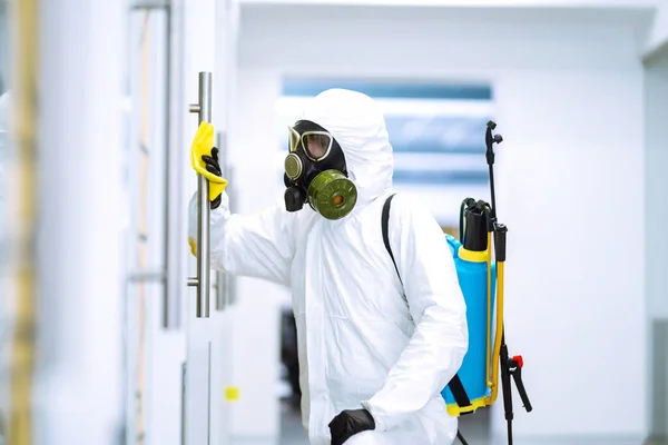 Man in protective hazmat suit washes door handles in office to preventing the spread of coronavirus, pandemic in quarantine city. Cleaning and disinfection of office. Covid-19.