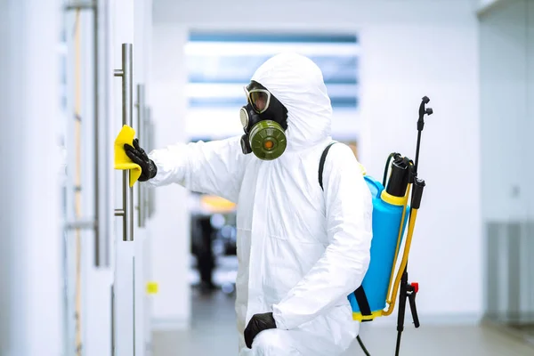Man in protective hazmat suit washes door handles in office to preventing the spread of coronavirus, pandemic in quarantine city. Cleaning and disinfection of office. Covid-19.