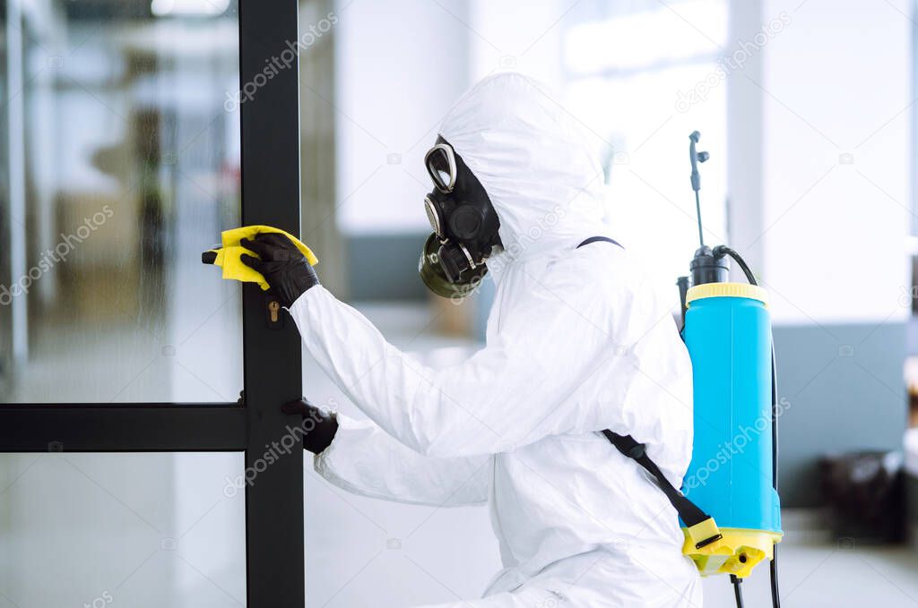 Man in protective hazmat suit washes door handles in office to preventing the spread of coronavirus, pandemic in quarantine city. Cleaning and disinfection of office. Covid-19.