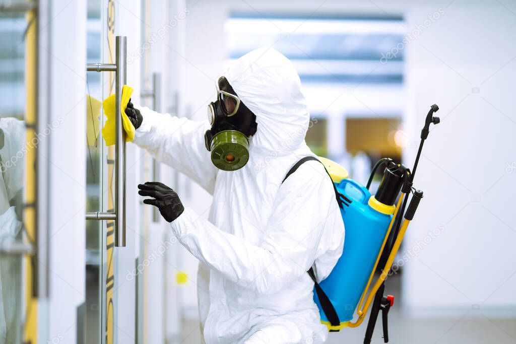 Man in protective hazmat suit washes door handles in office to preventing the spread of coronavirus, pandemic in quarantine city. Cleaning and disinfection of office. Covid-19.