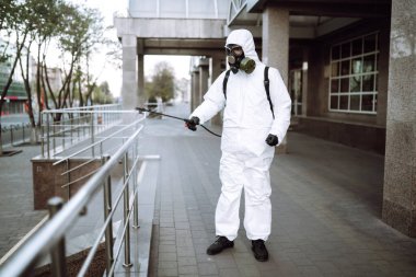 Koruyucu giysili ve maskeli bir adam şafak vakti karantina şehrindeki boş halka açık alanda dezenfektan sıkar. Covid -19. Temizlik kavramı.