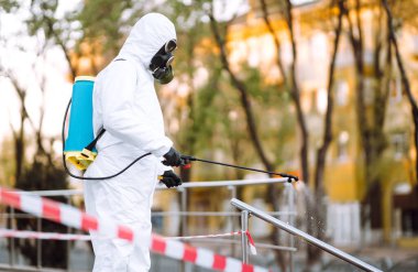 Koruyucu giysili ve maskeli bir adam şafak vakti karantina şehrindeki boş halka açık alanda dezenfektan sıkar. Covid -19. Temizlik kavramı.