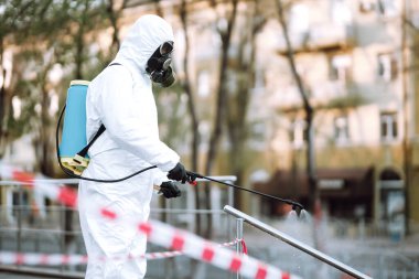Koruyucu giysili ve maskeli bir adam şafak vakti karantina şehrindeki boş halka açık alanda dezenfektan sıkar. Covid -19. Temizlik kavramı.