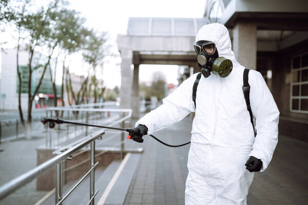 Человек в защитном костюме и маске дезинфицирует перила в пустом общественном месте на рассвете в городе карантина. Ковид - 19. Концепция очистки
.
