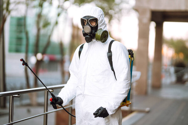 Человек в защитном костюме и маске дезинфицирует перила в пустом общественном месте на рассвете в городе карантина. Ковид - 19. Концепция очистки
.