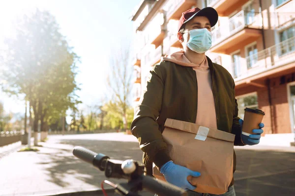 スクーターの保護マスクと医療用手袋の宅配便は 食品とクラフト紙パケットを提供します 隔離下での配送サービス 病気の発生 コロナウイルスCovid 19パンデミック条件 — ストック写真