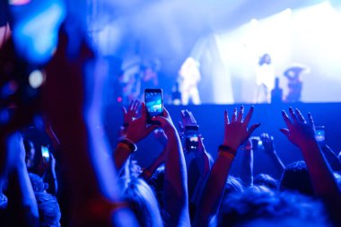 İnsanlar müzik festivali sırasında akıllı telefonlarıyla fotoğraf çekiyorlar. Taraftarlar ışık gösterisi ve alkışlarla rock konserinin keyfini çıkarıyorlar.