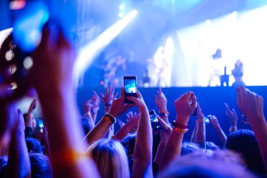İnsanlar müzik festivali sırasında akıllı telefonlarıyla fotoğraf çekiyorlar. Taraftarlar ışık gösterisi ve alkışlarla rock konserinin keyfini çıkarıyorlar.
