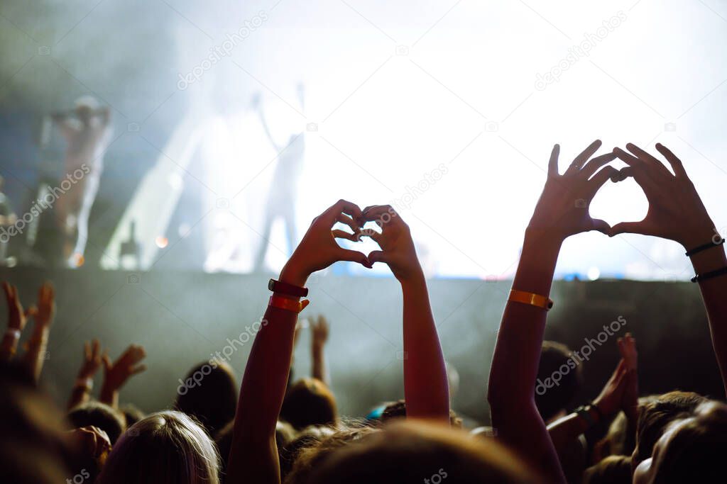 Heart shaped hands at concert, loving the artist and the festival. Music concert with lights and silhouette of people enjoying the concert.