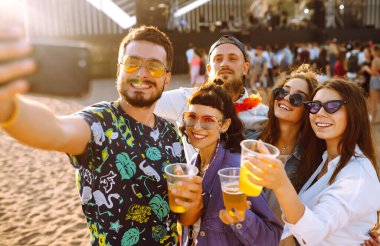 Genç mutlu arkadaşlar bira içiyor ve müzik festivalinde birlikte eğleniyorlar. Plaj partisi, yaz tatili, tatil konsepti. Arkadaşlık ve kutlama konsepti.