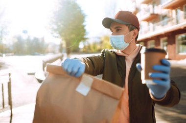 Karantina şehrinde kurye bir çanta yiyecek ve kahve getiriyor. Teslimat hizmeti konsepti. Covid 2019.